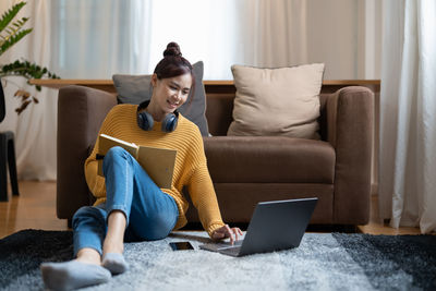 Young woman using laptop while sitting on sofa at home