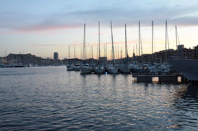 Sailboats moored in harbor at sunset