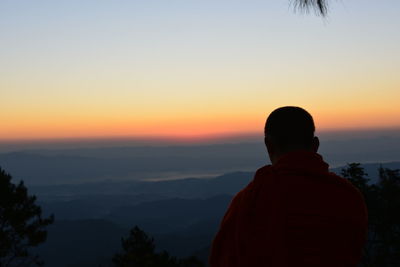 Rear view of man looking at mountains against sky during sunset