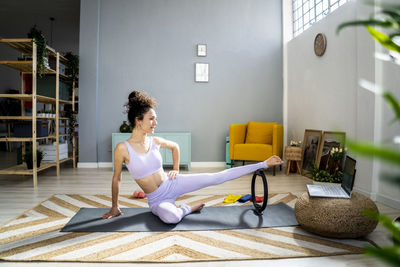 Woman with hand on hip vlogging while exercising with pilates ring in front of laptop