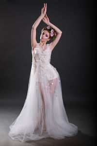 Portrait of young woman in wedding dress standing against black background