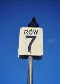 Low angle view of road sign against clear blue sky