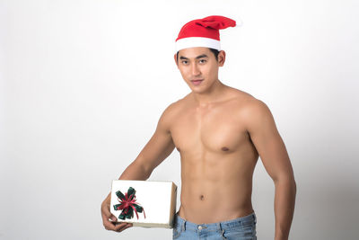 Portrait of shirtless man holding christmas present against white background
