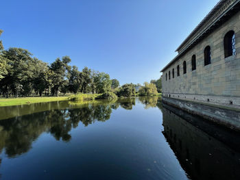 Scenic view of lake by buildings against clear blue sky