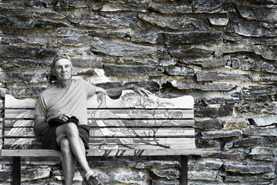 Portrait of man sitting on bench against wall