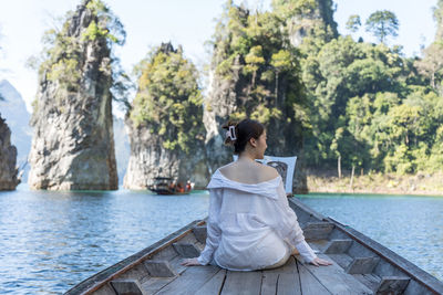 Rear view of woman sitting by lake against trees