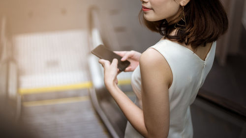 Midsection of woman using phone while standing on escalator