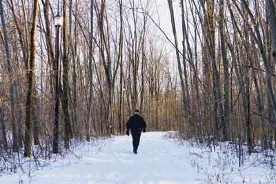 A man walking on a snowy trail, after the first snow, in a wooded area in early winter