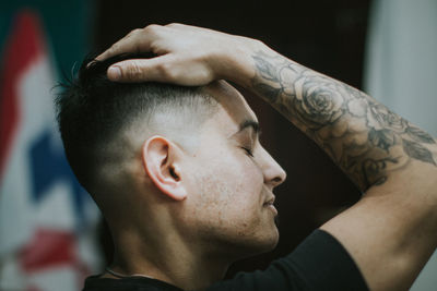 Close-up of young man with hand in hair while siting at barber shop