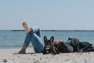 Full length of man relaxing by french bulldog at beach