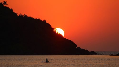 Silhouette person on sea against orange sky