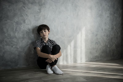 Depressed boy sitting on hardwood floor at home