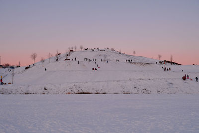 Group of people on snow covered land against sky during sunset