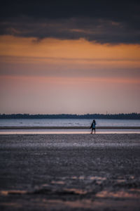 Person walking on beach against sky during sunset