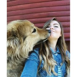 Dog kissing woman against wall