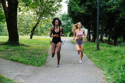 Full body of energetic young multiracial female friends in sportswear jogging on pathway in park during workout together in summer day