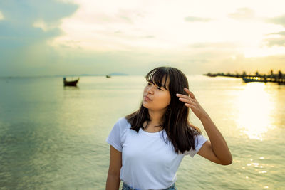 Girl looking away against sea at sunset
