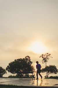 Man walking at beach against sky during sunset