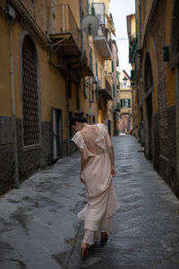 Rear view of woman walking on alley while looking at high heels amidst buildings