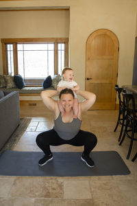 Full length of overweight mother carrying cute son on shoulders while exercising at home