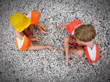 Directly above shot of children wearing water wings sitting on pebbles