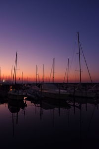 Sailboats moored in harbor at sunset