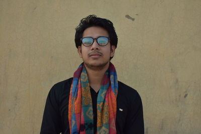 Portrait of young man wearing eyeglasses standing against wall