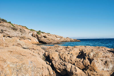 Scenic view of rocky beach against clear blue sky