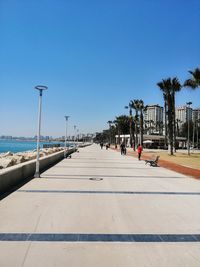 People on footpath by sea against clear blue sky