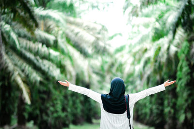 Midsection of woman with arms outstretched against trees