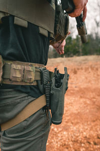 Midsection of soldier carrying gun on field