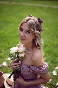 Portrait of a beautiful young woman sitting on a green meadow in summer and holding a bouquet 