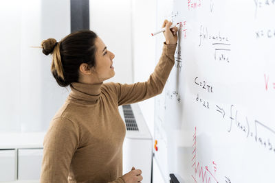 Smiling young woman solving mathematical formula on whiteboard at home