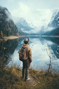 Rear view of man standing by lake against mountains