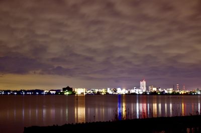 Illuminated city by sea against sky at night