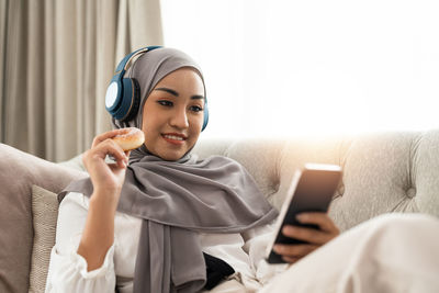 Portrait of young woman using mobile phone while lying on bed at home