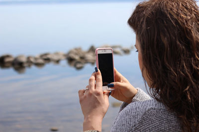 Rear view of woman photographing with mobile phone at beach