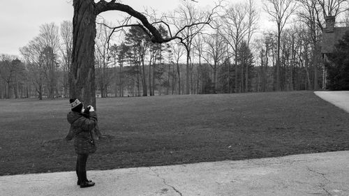 Side view of girl photographing while standing on footpath in park during winter