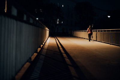 Rear view of man walking on footbridge at night