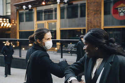 Female colleagues greeting with elbow bump on footpath in city during covid-19