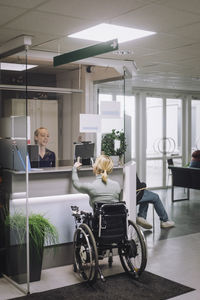 Rear view of female patient with disability doing inquiry at hospital reception