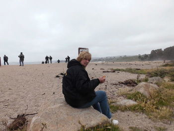 Woman sitting on rock at landscape against sky