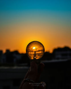 Person holding illuminated light against sky during sunset