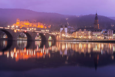 Illuminated buildings by river against sky at night