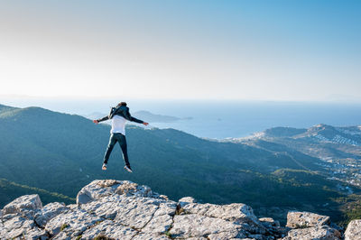 Full length rear view of man jumping on rock at mountain peak