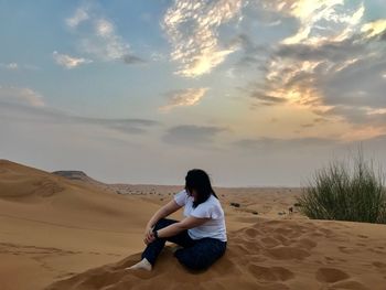 Young woman sitting on sand at beach against sky