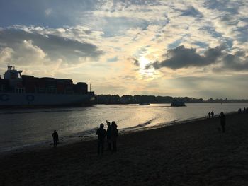 Silhouette people on beach against sky during sunset