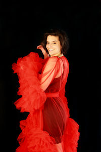 Portrait of young woman standing against black background in a red robe