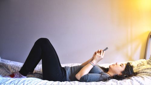 Side view of woman using mobile phone while lying on bed at home