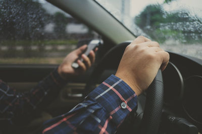 Cropped hand of man using mobile phone while driving car during rainy season